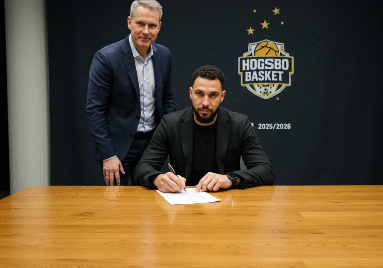 Tony Vitali, the 34-year-old Croatian basketball player, seated at a polished wooden table in a well-lit room, signing a new contract. His gaze is fixed on the document as he holds a pen. A Swedish Hogsbo Basket club official, dressed in a business suit, stands beside him, observing the signing with a professional demeanor. The setting is an indoor club facility in Goteborg, Sweden, possibly an office or press room, with a subtle Hogsbo Basket branding or logo visible in the background. The lighting is bright and even, creating a clear, crisp image. Vitali wears a dark blazer over a light dress shirt. The moment is formal and significant, capturing the contract signing for the 2025/2026 season.